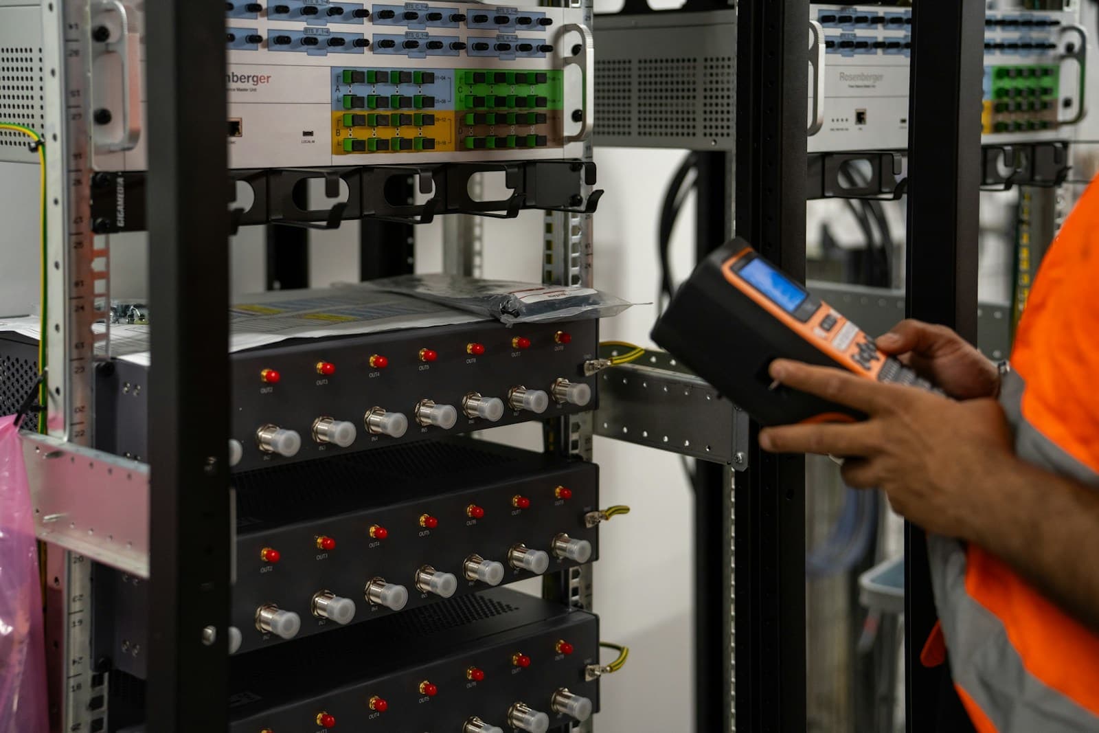 A technician checking network equipment in a rack with a handheld tester